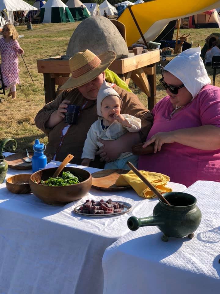 Two women and a baby sitting outdoors at a table for a medieval feast